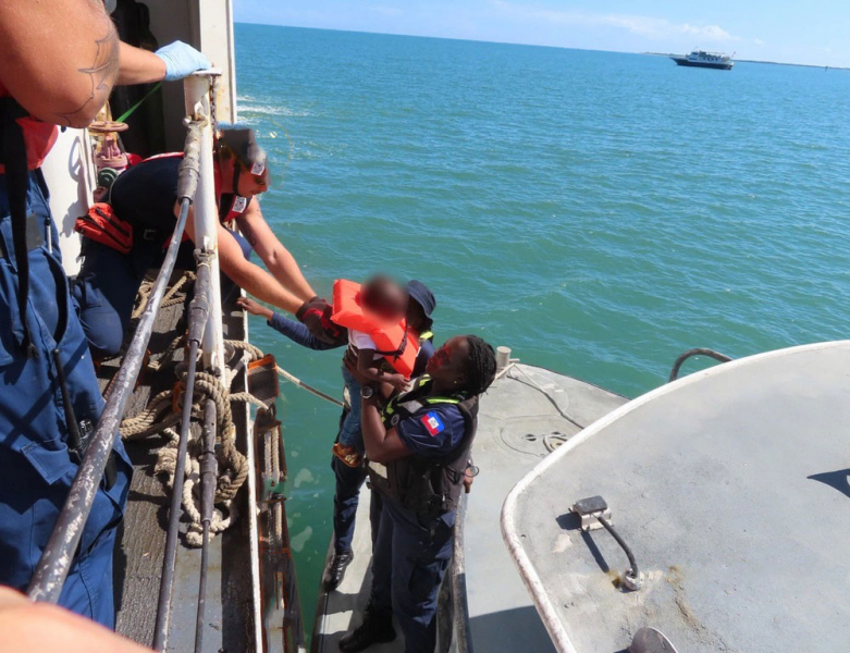 A child who was rescued at sea off a boat of migrants is handed back to the Haitian authorities by the US Coast Guard.