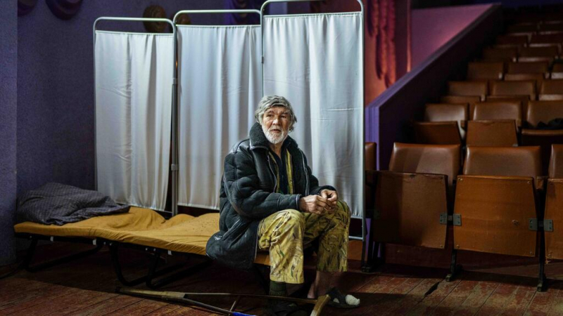 Elderly Ukrainian refugee sits in a theater-turned-shelter amid ongoing war.
